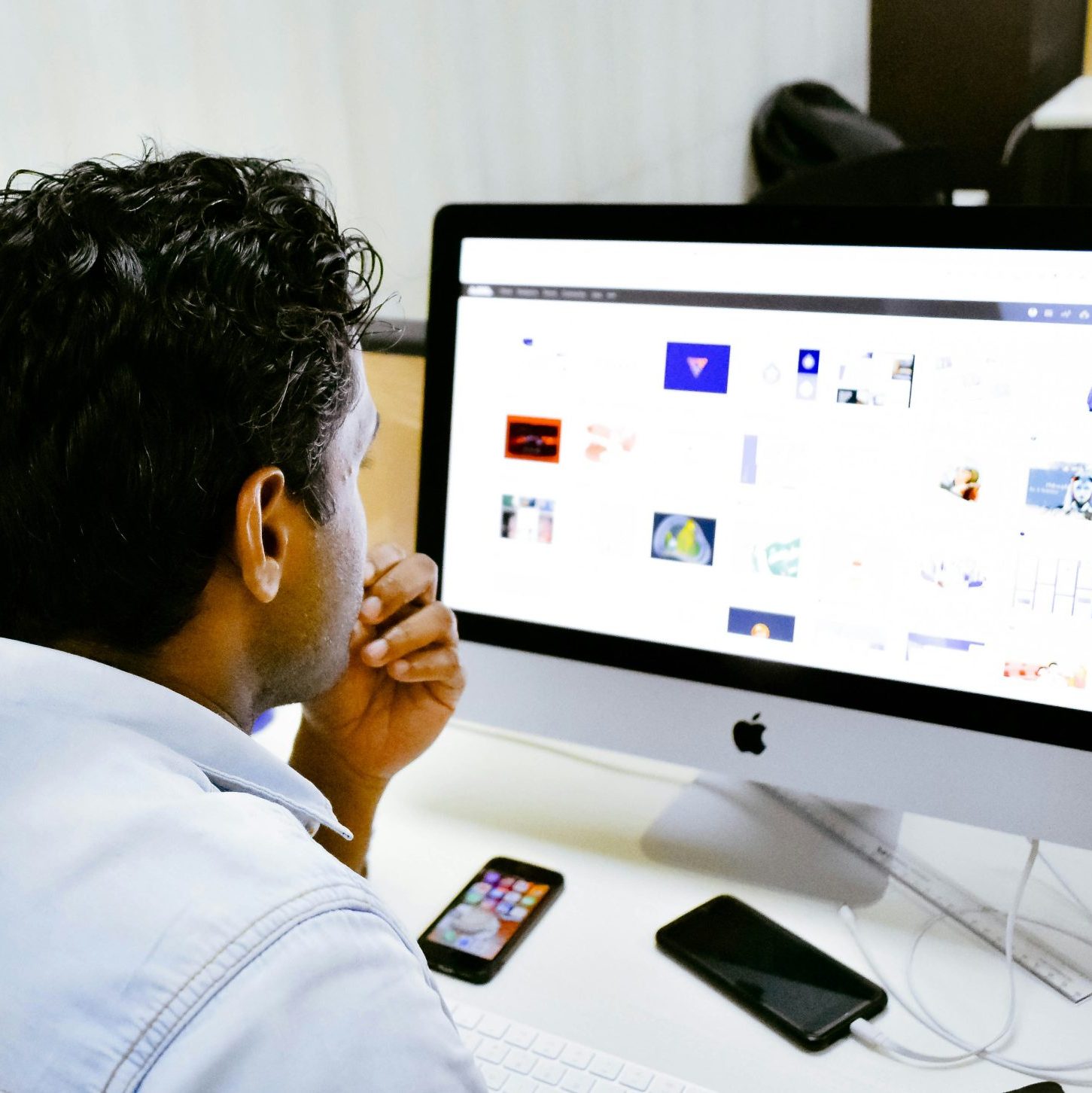 man sitting in front of silver Apple iMac on table